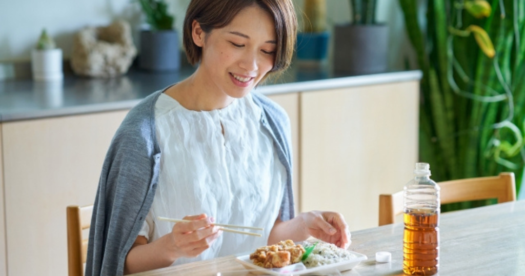 テーブルでパック入りの惣菜を食べる女性