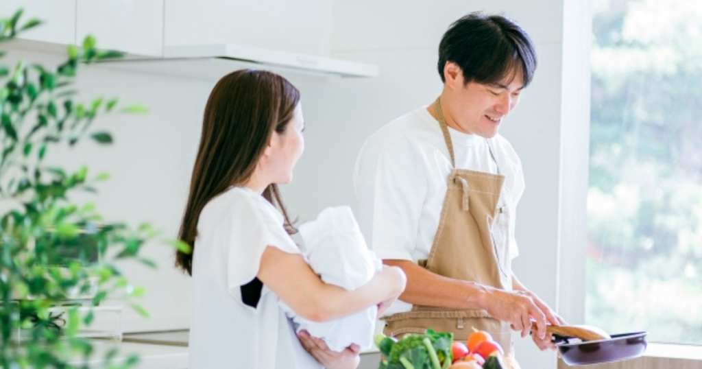 キッチンで料理をするパートナーと赤ちゃんを抱いてそばに立つ女性