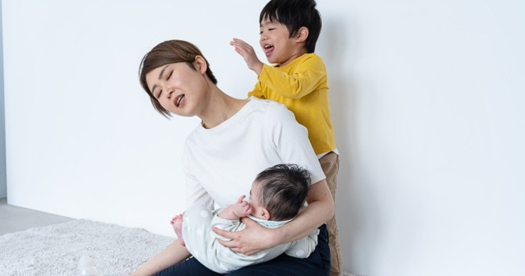 赤ちゃんを抱っこしながら上の子に抱きつかれて疲れた様子の女性